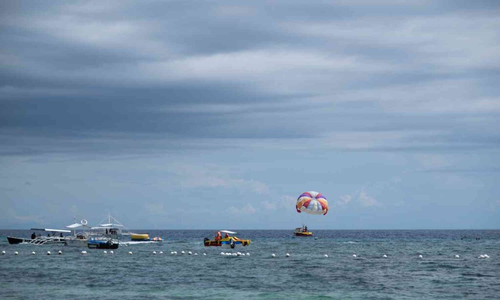 Parasailing and boats off the coast of Bohol, Philippines under cloudy skies