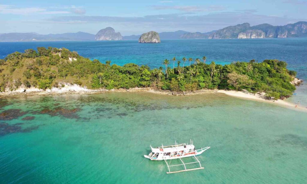 Traditional boat in clear tropical waters beside a small island in the Philippines