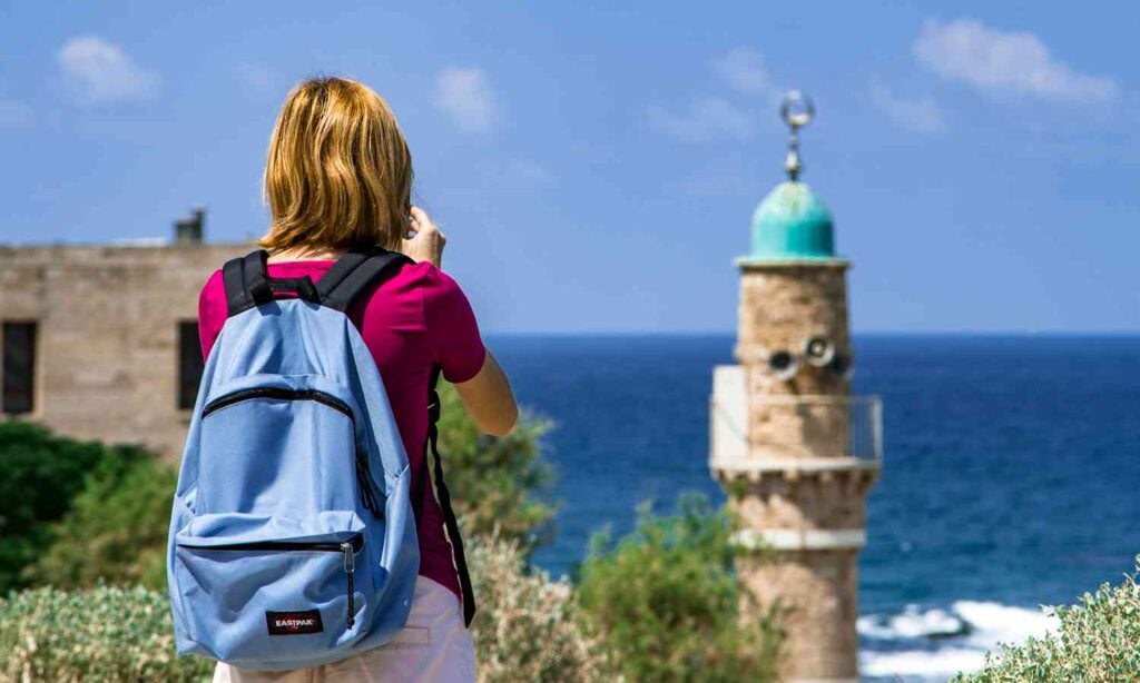 Traveler photographing historic Jaffa with a mosque minaret and the Mediterranean Sea in the background